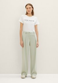 Witte T-shirt met de tekst "TOM TAILOR EST. 1962", gecombineerd met lichtgroene wijde broek met plooien en een knoopsluiting.