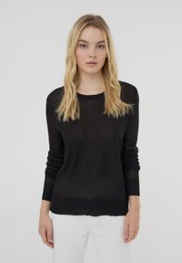 Maglione nero a maglia con scollo rotondo e polsini a coste. Tessuto semi-trasparente, vestibilità rilassata, abbinato a pantaloni bianchi.