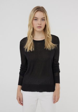 Maglione nero a maglia con scollo rotondo e polsini a coste. Tessuto semi-trasparente, vestibilità rilassata, abbinato a pantaloni bianchi.