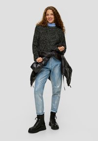 Zwarte textuurtrui, lichtblauwe coltrui eronder, lichtblauwe jeans en zwarte chunky laarzen, met een zwarte pufferjack om de taille geknoopt.