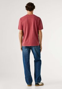 Camiseta roja de algodón con mangas cortas, cuello redondo y dobladillo recto, combinada con vaqueros azules de mezclilla. Diseño simple y casual.