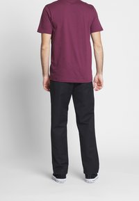 Bordowa bawełniana koszulka z krótkim rękawem w zestawieniu z czarnymi spodniami. Spodnie mają prosty krój i są noszone z czarnymi sneakersami.