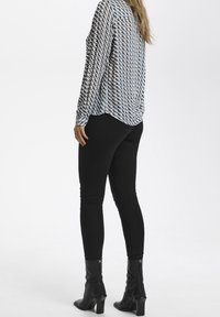 Camicia a maniche lunghe con fantasia in blu, bianco e beige, abbinata a leggings neri e stivali neri con tacco, vista da dietro.