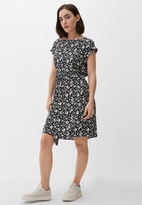 Czarna i biała sukienka w panterkę z krótkimi rękawami, z wiązaniem w talii i delikatnie rozszerzanym dołem, w połączeniu z beżowymi sneakersami.