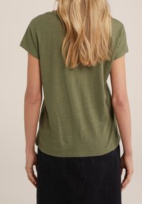 Camisa de tirantes de color verde oliva con un corte holgado, dobladillo redondeado y textura suave, combinada con una falda oscura.