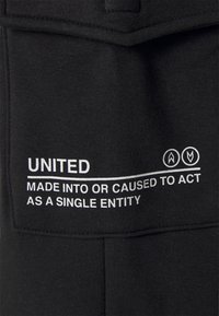 Svart tyg med vit text som säger "ENHETLIGT GJORD FÖR ATT HANDLA SOM EN ENDA ENHET." Slät yta, inga synliga mönster eller detaljer.