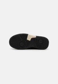 Semelle en caoutchouc noire avec des motifs texturés, comprenant des designs circulaires et en zigzag. Un accent beige se trouve au centre.