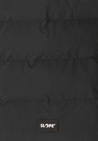 Svart pufferjacka med quiltad design, med en framträdande logopatch och en slät, något glansig yta.