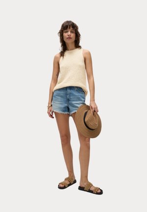 Beige Strick-Top, zerrissene Denim-Shorts, brauner, breitkrempiger Strohhut und braune Riemchensandalen mit Nieten. Lässiges Sommeroutfit.