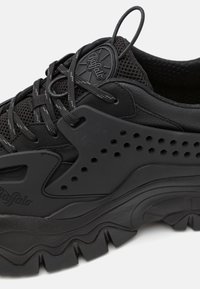 Sneaker noir arborant une combinaison de matériaux en maille et en caoutchouc, des détails texturés et une semelle épaisse et sculptée avec un relief prononcé.