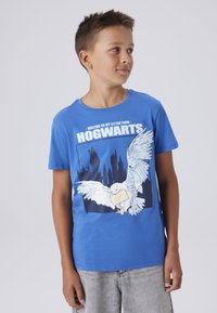 Camiseta de algodón azul con un gráfico blanco de un búho sosteniendo una carta, y el texto "ESPERANDO MI CARTA DE HOGWARTS" en fuente blanca en negrita.