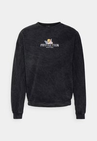 Felpa nera in cotone con maniche lunghe, scollo rotondo e testo ricamato "PROTECTION KAOTIKO" accompagnato da un design grafico.