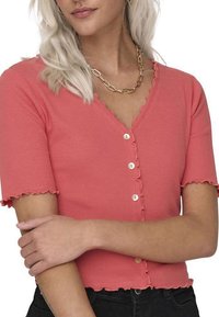 Cardigan court à manches courtes en corail à côtes avec un col et un ourlet en forme de vagues, orné de boutons ronds sur le devant. En mélange de coton léger.