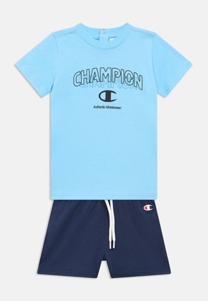 T-shirt azzurro cielo a maniche corte con scritta e logo "CHAMPION", abbinata a pantaloncini blu navy con coulisse e piccolo logo Champion.