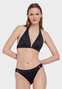 Černý bikiny set s trojúhelníkovým halter krkem, hlubokým výstřihem do V a odpovídajícími kalhotkami nízkého střihu se postranními detaily. Hladká textury látky.