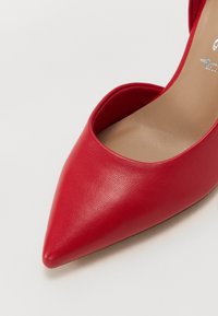 Chaussure à talon haut en cuir rouge avec un bout pointu et un design à côté ouvert ; texture lisse avec une semelle intérieure beige neutre.
