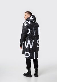 Czarny pikowany płaszcz z białym nadrukiem literowym, kapturem i długim krojem. Posiada prążkowane mankiety i boczne kieszenie. Noszony z czarnymi spodniami i botkami.