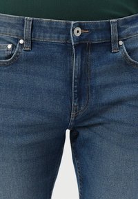 Jean en denim bleu avec une taille mi-haute, dotés de quincaillerie en métal argenté, de détails de couture subtils et d'un design classique à cinq poches.