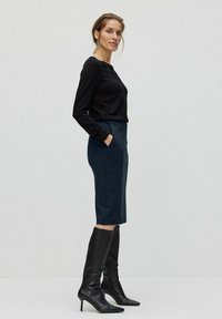 Svart långärmad topp i kombination med en knälång, marinblå pennkjol med sidfickor och en figurnära design. Bärs med knähöga svarta stövlar.