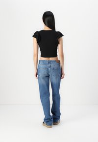 Top negro de manga corta con detalles de volantes, combinado con jeans de corte holgado azul claro que presentan un diseño de cinco bolsillos y una etiqueta de cuero en la parte trasera.