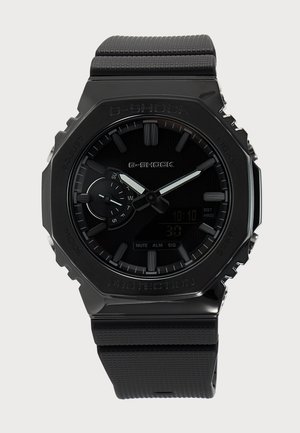 Reloj de pulsera G-Shock negro con correa texturizada, pantalla analógica y digital, subesfera del día de la semana, y manecillas luminosas de hora y minutos.
