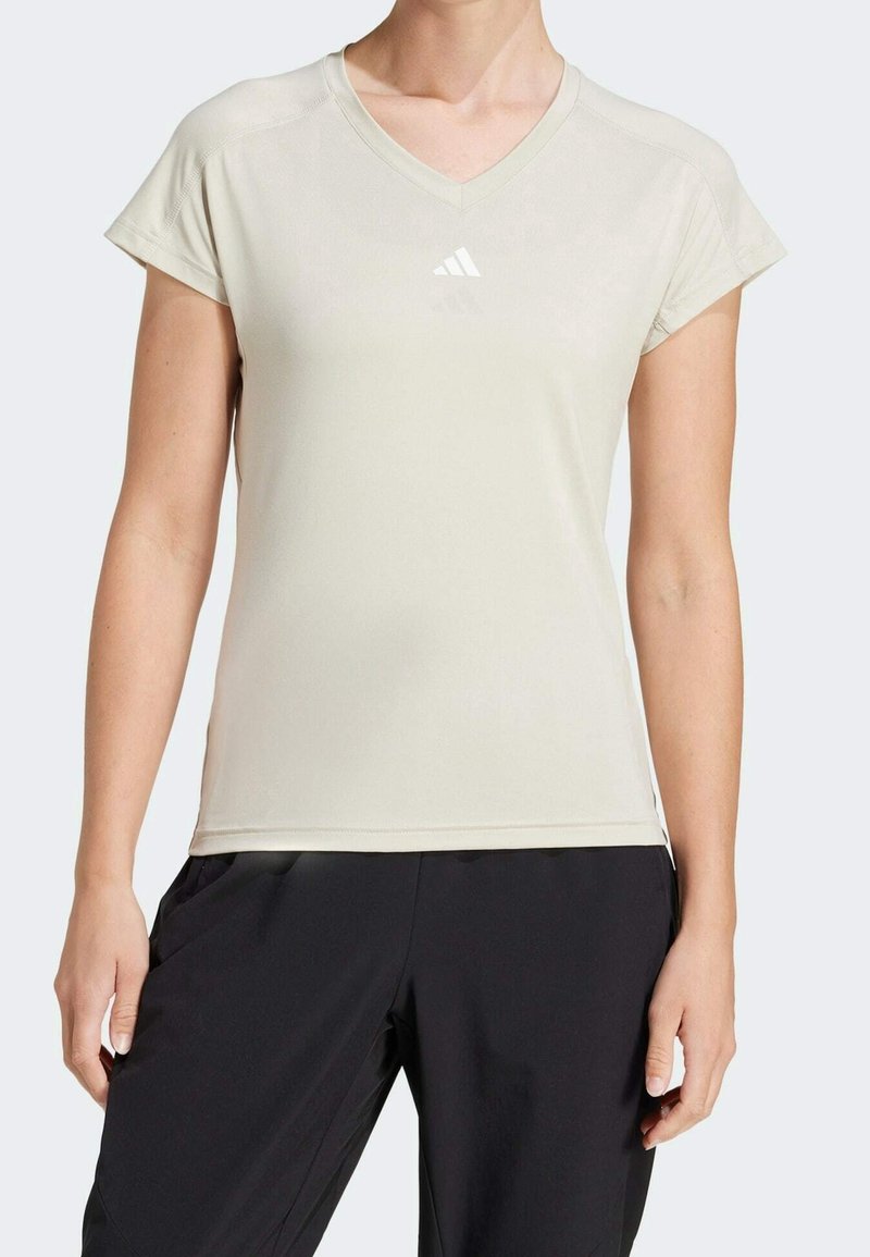 Ljusbeige atletisk t-shirt i fukttransporterande tyg, med V-hals, korta ärmar och en liten vit logotyp på bröstet.