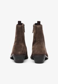 Botas de tobillo de ante marrón con un tacón bajo, que cuentan con una cremallera lateral y acentos elásticos en contraste en la parte superior para mayor comodidad al ponérselas.