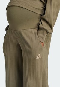 Olivgrön ribbad gravidbyxor med sidofickor och en metallisk Adidas-logotyp på vänster lår. Mjuk textur, avslappnad passform.