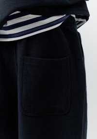 Zbliżenie na kieszeń granatowych polarowych spodni pod paskowanym, granatowo-białym dołem koszuli.