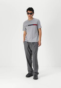Grå t-shirt med horisontale røde og hvide striber, med teksten "TOMMY HILFIGER". Sammen med løse grå bukser og sorte sneakers.