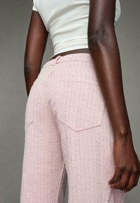 Ljust rosa, texturerade jeans med hög midja, två bakfickor och fransade fållar, sammansatta med en vit, figurnära topp.