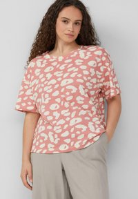 T-Shirt mit pinkem Leopardenmuster in lockerer Passform und kurzen �Ärmeln. Weicher Stoff, runder Halsausschnitt und abgerundeter Saum. Kombiniert mit hellgrauen Hosen.