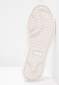 Vit sneakersula med texturerat greppmönster, med en framträdande böjd design och släta kanter, visad mot en ljus bakgrund.