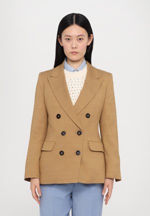 Brown double-breasted blazer with black buttons, notch lapels, two front pockets, textured fabric, layered over a light sweater and shirt.