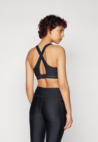 Svart sportsbh med kryssryggdesign, med en logobånd og en høy midjebånd på glatte, tettsittende svarte leggings.