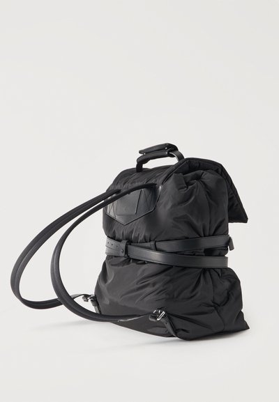 Μαύρο σακίδιο πλάτης από νάιλον με επάνω λαβή, ρυθμιζόμενους ιμάντες ώμου και φαρδιά λεπτομέρεια δερμάτινης ζώνης γύρω από τη μέση.