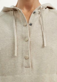 Felpa con cappuccio beige caratterizzata da una mezza chiusura a bottoni con bottoni color sabbia, tessuto a maglia testurizzato e lacci visibili a livello del collo.