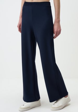 Navy brede-pijpen broek van zachte stof, voorzien van een elastische tailleband en zijkanten voor extra detail. Gepaard met witte sneakers.