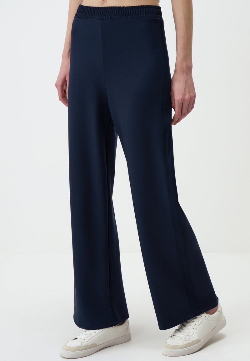 Navy brede-pijpen broek van zachte stof, voorzien van een elastische tailleband en zijkanten voor extra detail. Gepaard met witte sneakers.