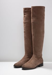 Brązowe zamszowe kozaki do kolan o gładkiej fakturze, z ostrym noskiem, niskim blokowym obcasem oraz zamkiem błyskawicznym po wewnętrznej stronie.