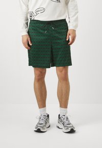 Grønne badshorts med mønster og elastisk talje med snor. Har geometrisk design og går til lige over knæet. Kombinationen med sneakers.