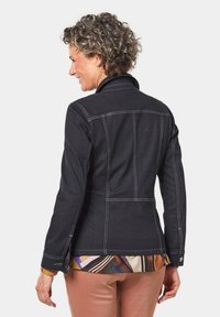 Schwarze Jeansjacke mit weißen Nähten, taillierter Schnitt und Kragen. Sie hat einen abgerundeten Saum und Knopfdetails an den Bündchen.