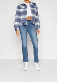 Kappad blå och vit rutiga jacka med en vit fårskinnskrage, kombinerad med ljusblå raka jeans och vita sneakers.