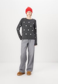 Gray knitted sweater with white heart patterns, paired with gray wide-leg jeans and tan boots. Model wears a bright red knit beanie.