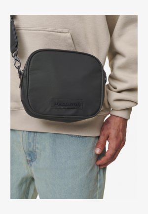 Zwarte schoudertas van glad materiaal, rechthoekige vorm, met een logo-patch aan de voorkant, ritssluiting en een verstelbare schouderband.