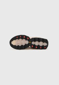 Semelle d'une chaussure beige avec une bande de roulement noire et translucide, présentant des crampons circulaires rouges et un petit logo jaune au centre.