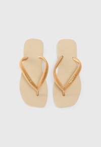 Infradito beige con suole testurizzate, morbide cinghie in stoffa color sabbia e dettagli in oro con il nome del marchio "havaianas".