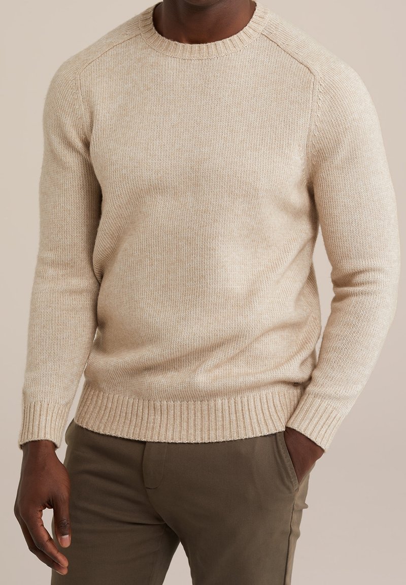 Béžový pletený svetr s žebrovaným kulatým výstřihem a manžetami, s texturovaným povrchem. Nosit s olivově zelenými kalhotami.