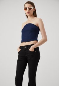 Top crop sin mangas de color azul marino hecho de tela texturizada, combinado con jeans negros ajustados que cuentan con un diseño clásico de cinco bolsillos.