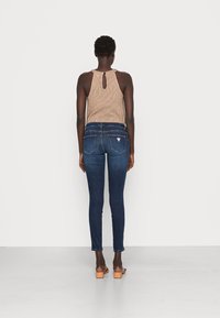Vaqueros skinny azul oscuro con costuras en contraste y dos bolsillos traseros. Combinados con una camiseta sin mangas de textura beige que presenta un escote en forma de llave en la parte posterior.